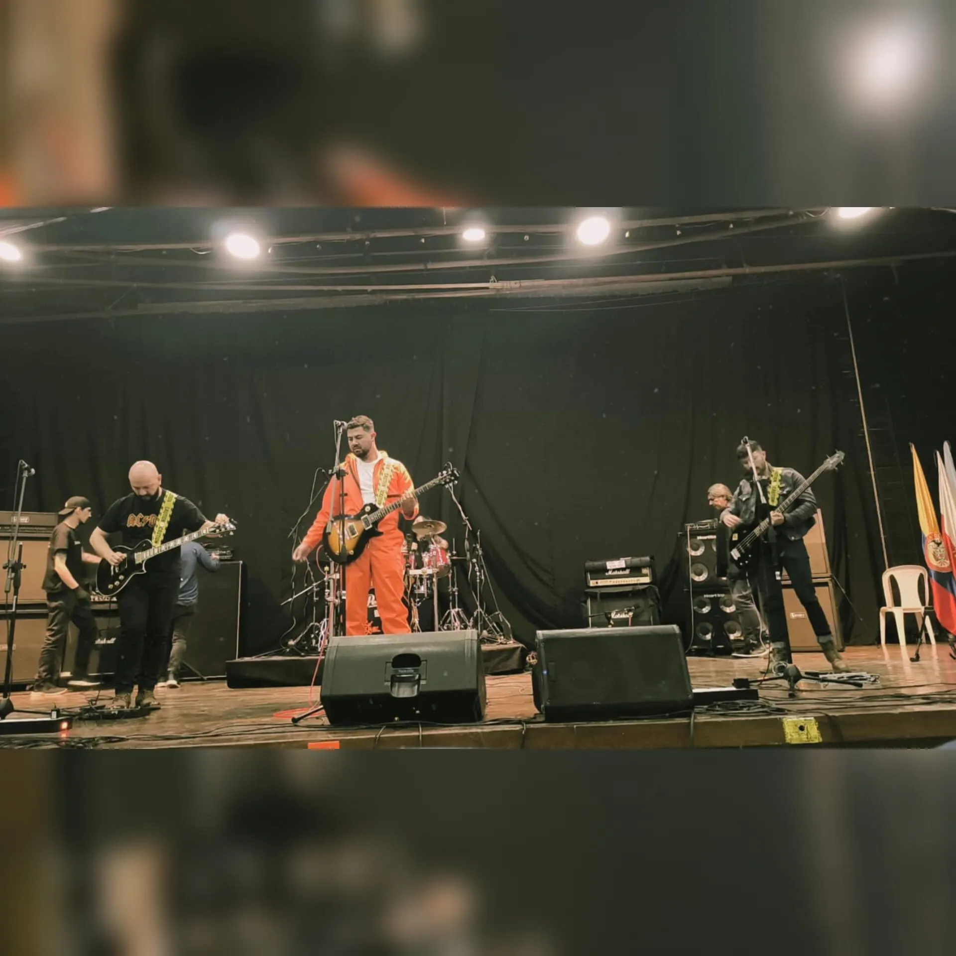 Vocalista con overol naranja en escenario formal