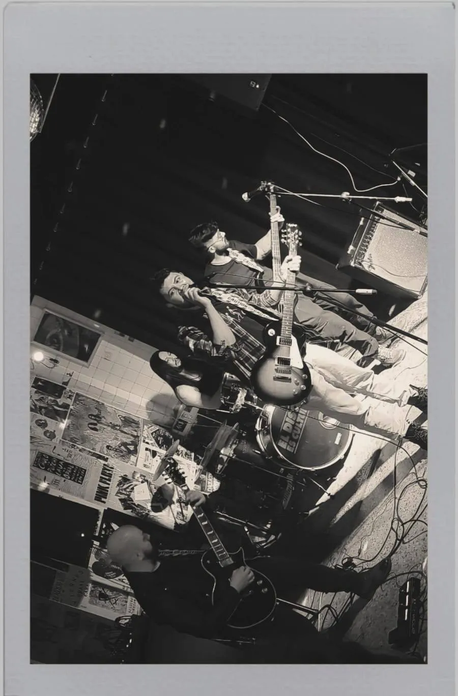 Polaroid de la banda en un local underground con afiches